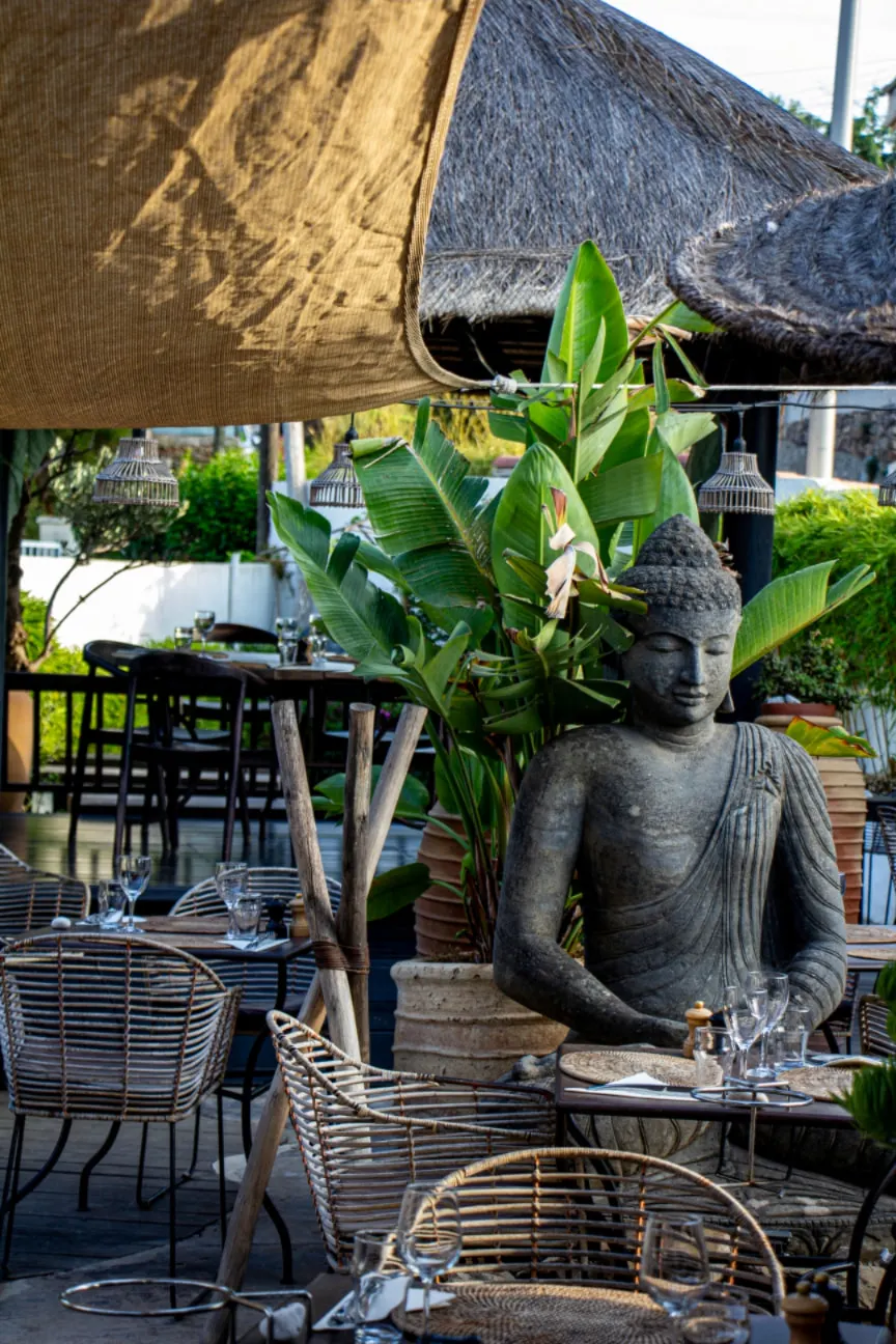 Statue de Bouddha au milieu des plantes et des tables en rotin sous les paillotes
