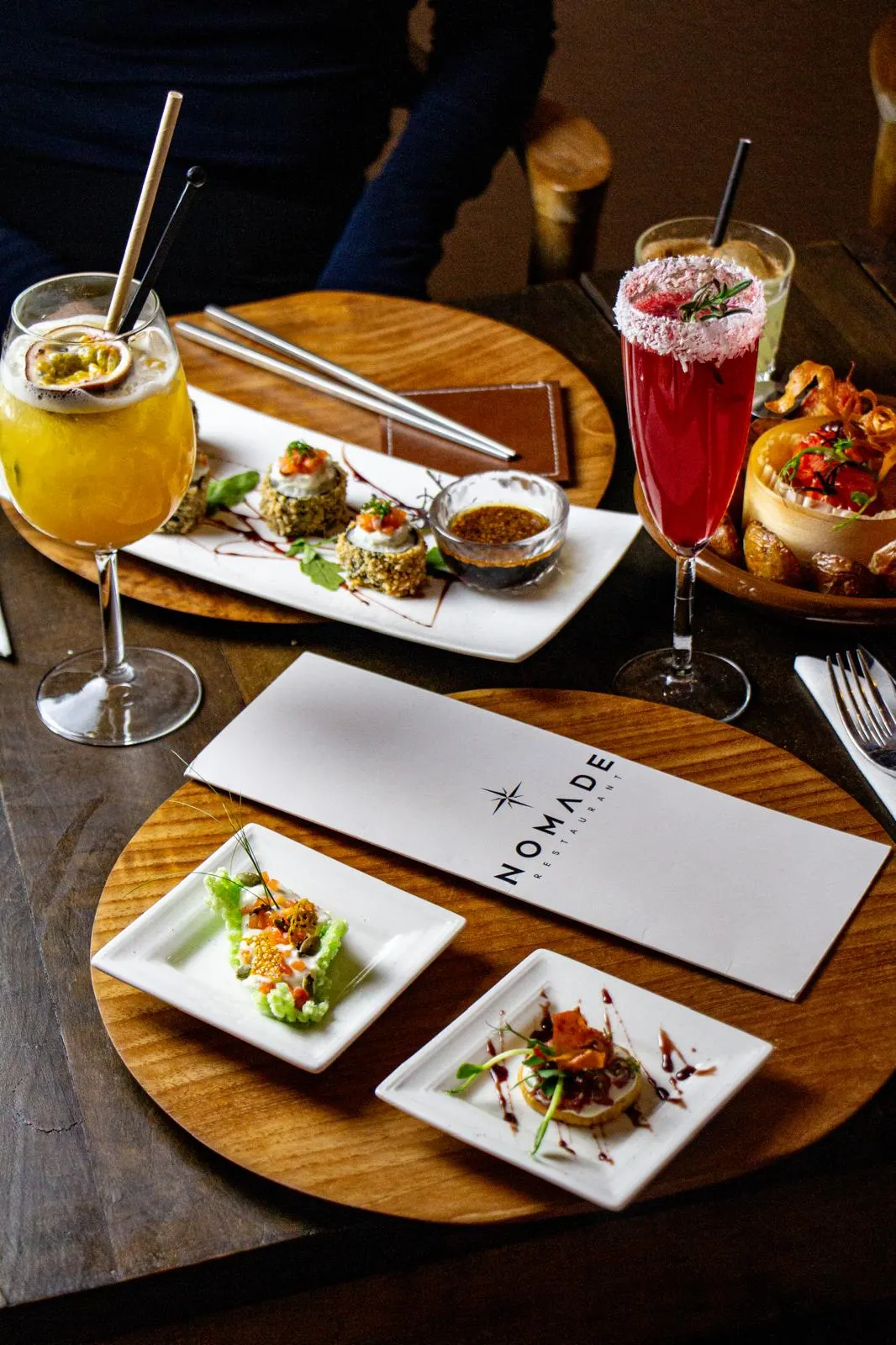 Deux cocktails, assiettes de tapas et carte Nomade sur une table en bois